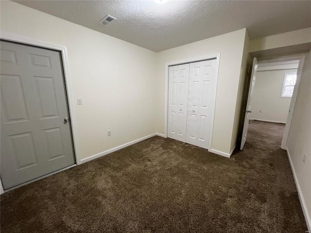 unfurnished bedroom with dark colored carpet, a textured ceiling, and a closet