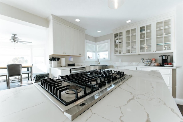 kitchen with white cabinets, ceiling fan, light stone counters, and sink