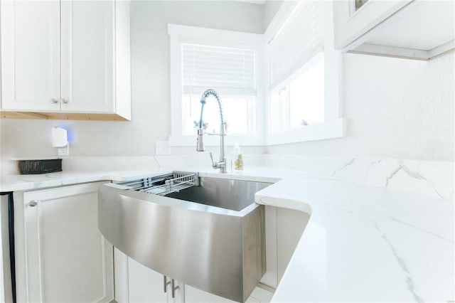 kitchen featuring light stone counters, white cabinetry, and sink