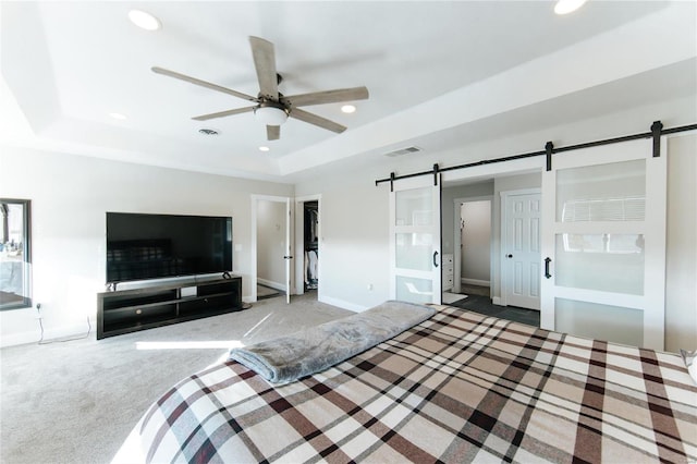 unfurnished bedroom featuring carpet, a barn door, a tray ceiling, and ceiling fan