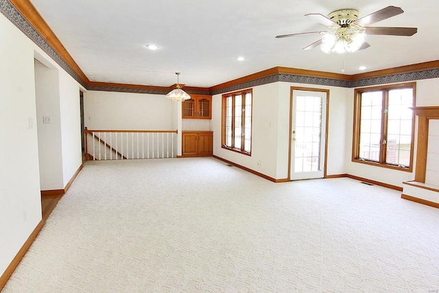 unfurnished living room with ceiling fan with notable chandelier, light carpet, and crown molding