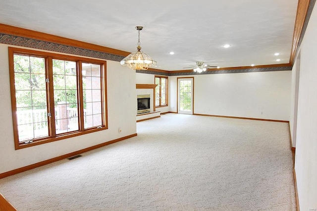 unfurnished living room with light colored carpet, plenty of natural light, ceiling fan with notable chandelier, and ornamental molding