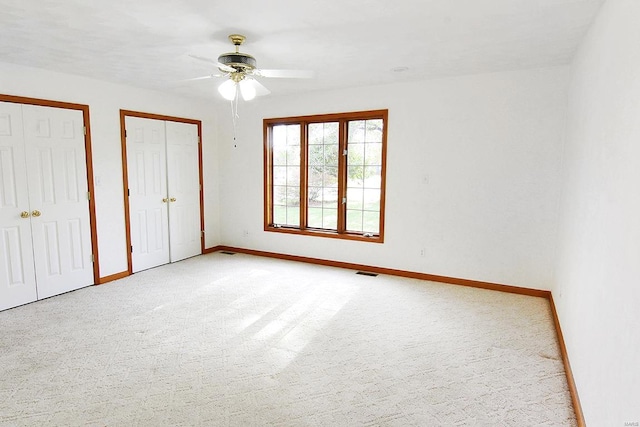 unfurnished bedroom featuring multiple closets, light colored carpet, and ceiling fan