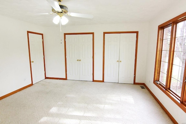 unfurnished bedroom featuring light carpet, two closets, and ceiling fan