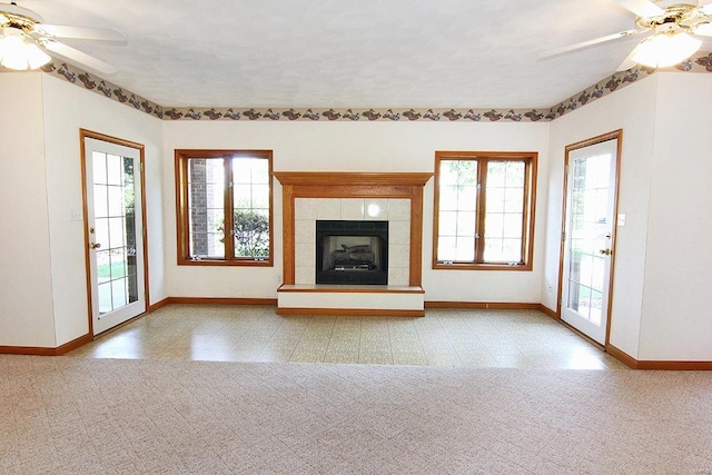 unfurnished living room featuring a tiled fireplace, a wealth of natural light, and ceiling fan