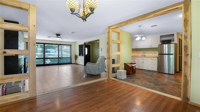 unfurnished living room with ceiling fan with notable chandelier and dark hardwood / wood-style flooring