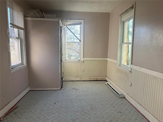 empty room with plenty of natural light, wooden walls, and a textured ceiling