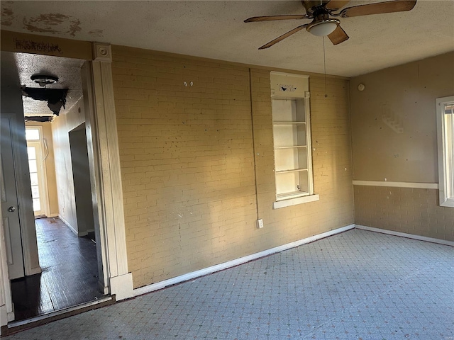 unfurnished room with brick wall, a textured ceiling, ceiling fan, and wood-type flooring