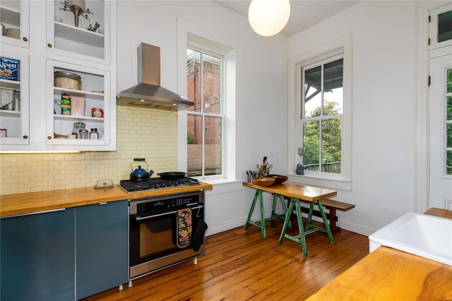 kitchen featuring wood-type flooring, white cabinets, decorative backsplash, wall chimney exhaust hood, and appliances with stainless steel finishes