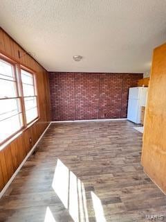 empty room featuring wood walls, a textured ceiling, hardwood / wood-style flooring, and brick wall