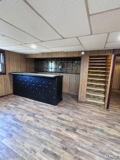 basement featuring a drop ceiling, wooden walls, and hardwood / wood-style floors