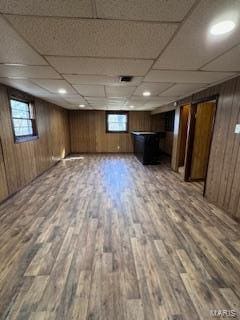 basement with a drop ceiling, wood-type flooring, and wood walls