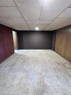 basement featuring a paneled ceiling, carpet flooring, and wooden walls