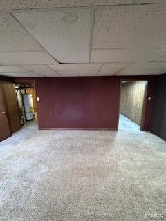 interior space featuring carpet floors, a paneled ceiling, gas water heater, and wood walls