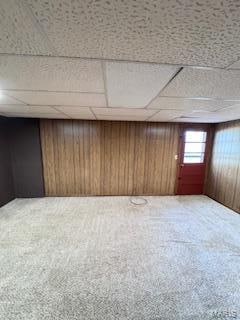 basement featuring carpet flooring, a paneled ceiling, and wooden walls