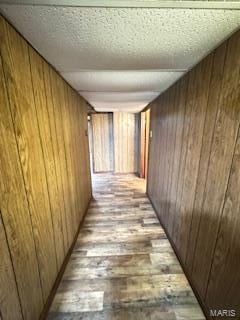 hall with a textured ceiling, light wood-type flooring, and wooden walls