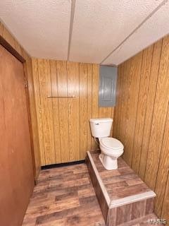 bathroom featuring wood walls, wood-type flooring, a textured ceiling, and toilet