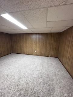 basement featuring wood walls, a paneled ceiling, and carpet floors