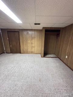 basement featuring wooden walls, a drop ceiling, and carpet