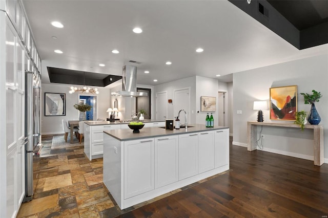 kitchen featuring sink, a notable chandelier, a kitchen island with sink, white cabinets, and exhaust hood