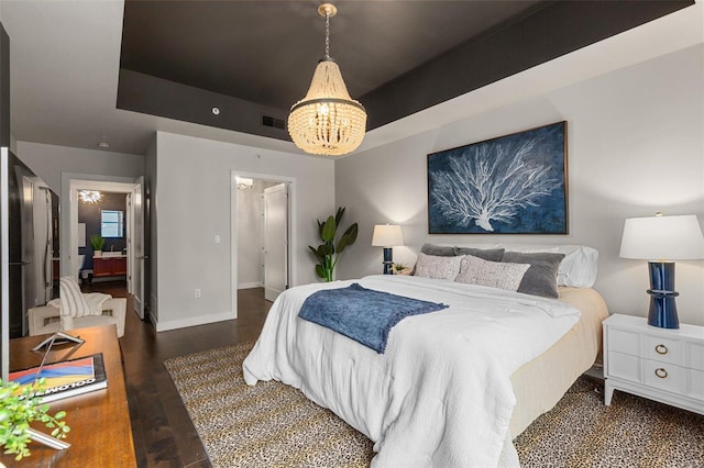 bedroom with dark hardwood / wood-style floors, an inviting chandelier, and a tray ceiling