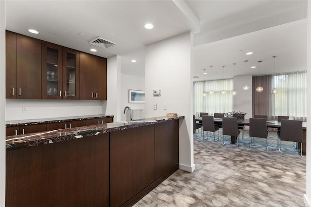 kitchen with dark brown cabinets, dark stone countertops, kitchen peninsula, and light carpet