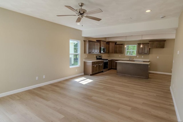 kitchen with appliances with stainless steel finishes, decorative light fixtures, dark brown cabinetry, light hardwood / wood-style flooring, and a center island