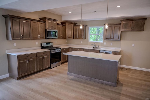 kitchen with stainless steel appliances, a kitchen island, hanging light fixtures, sink, and light hardwood / wood-style flooring