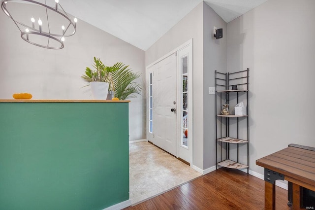 entryway with wood-type flooring, an inviting chandelier, and vaulted ceiling