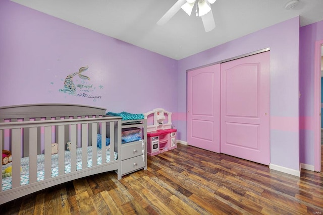 bedroom featuring a nursery area, dark wood-type flooring, ceiling fan, and a closet