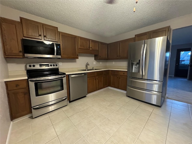 kitchen featuring a textured ceiling, stainless steel appliances, sink, and light tile patterned floors