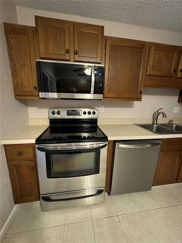 kitchen with light tile patterned flooring, a textured ceiling, sink, and appliances with stainless steel finishes