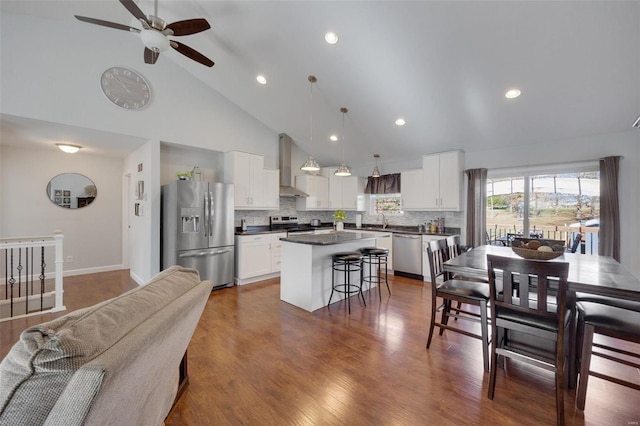 kitchen with pendant lighting, appliances with stainless steel finishes, white cabinets, wall chimney range hood, and a kitchen island