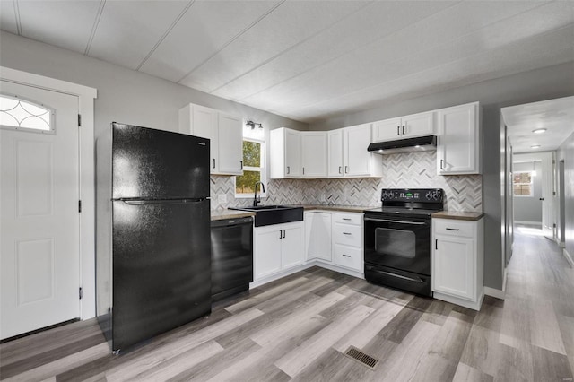 kitchen featuring backsplash, light hardwood / wood-style floors, white cabinetry, and black appliances