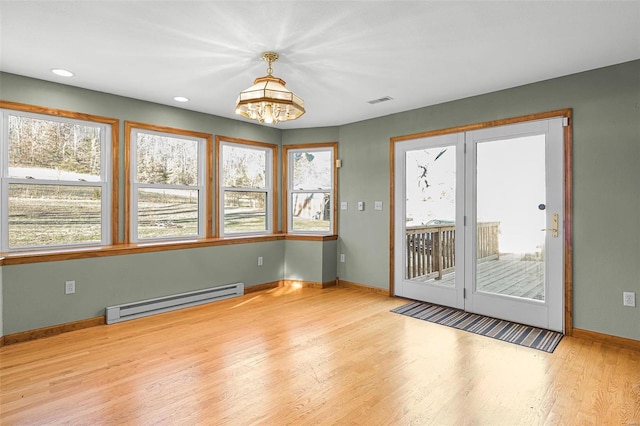 empty room featuring a chandelier, plenty of natural light, a baseboard radiator, and light hardwood / wood-style flooring