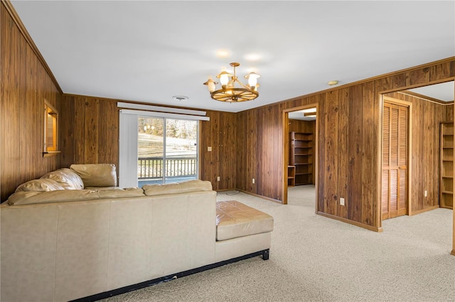 carpeted living room featuring wood walls, crown molding, and a chandelier