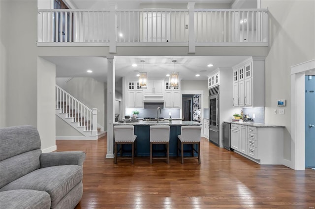 kitchen featuring pendant lighting, a high ceiling, white cabinets, dark hardwood / wood-style floors, and light stone counters