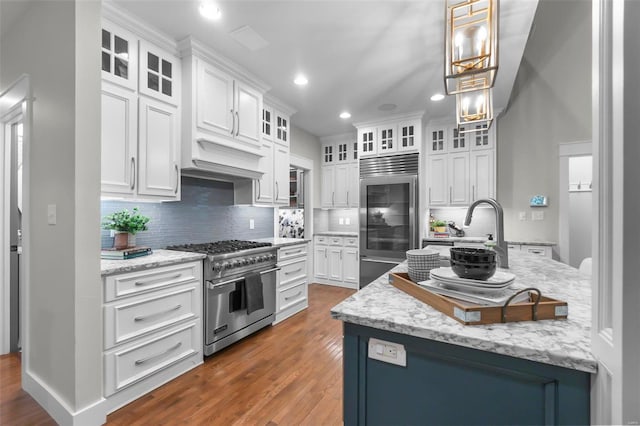 kitchen with decorative backsplash, premium appliances, pendant lighting, white cabinets, and dark hardwood / wood-style floors