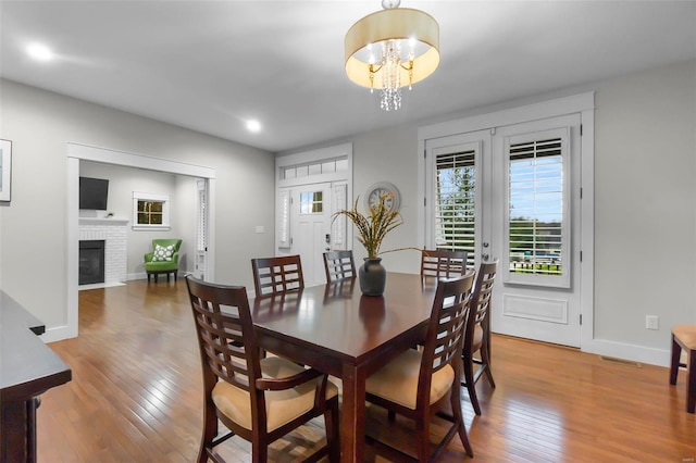 dining space featuring hardwood / wood-style floors, a chandelier, and a brick fireplace