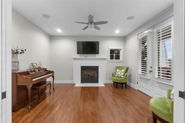 sitting room featuring ceiling fan, wood-type flooring, and a brick fireplace