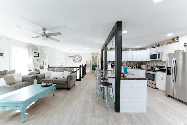 kitchen with a breakfast bar, ceiling fan with notable chandelier, light wood-type flooring, white cabinetry, and stainless steel appliances