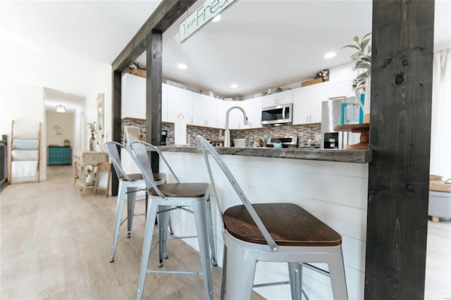 kitchen featuring a breakfast bar, decorative backsplash, light wood-type flooring, appliances with stainless steel finishes, and white cabinetry