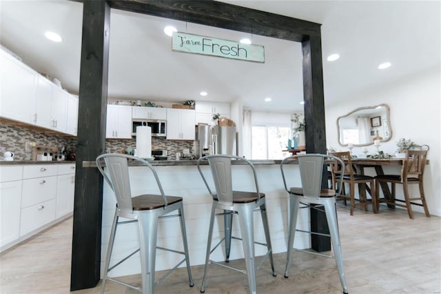 kitchen featuring backsplash, a kitchen breakfast bar, white cabinetry, and stainless steel appliances