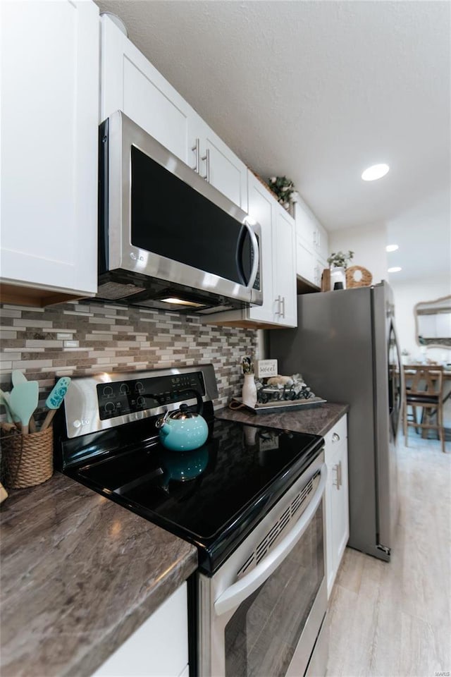 kitchen featuring decorative backsplash, stainless steel appliances, white cabinetry, and light hardwood / wood-style flooring