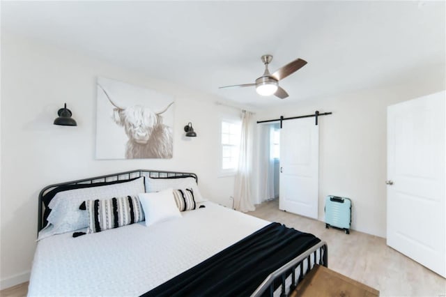 bedroom featuring ceiling fan, a barn door, and light hardwood / wood-style floors