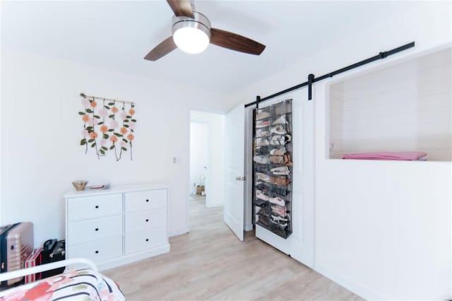 bedroom with a barn door, light hardwood / wood-style flooring, and ceiling fan