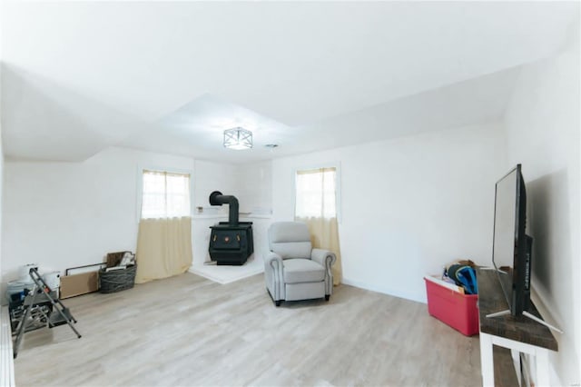 living area with a wood stove, light hardwood / wood-style flooring, and a wealth of natural light