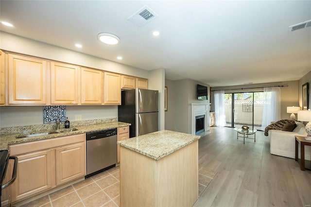 kitchen with stainless steel appliances, light brown cabinetry, light stone countertops, light hardwood / wood-style flooring, and a center island