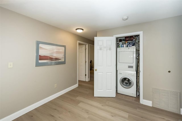 clothes washing area featuring stacked washing maching and dryer and light hardwood / wood-style flooring