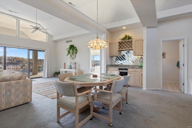 dining room featuring ceiling fan with notable chandelier, light colored carpet, and high vaulted ceiling